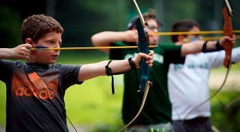 three youngs boys shooting a bow and arrow