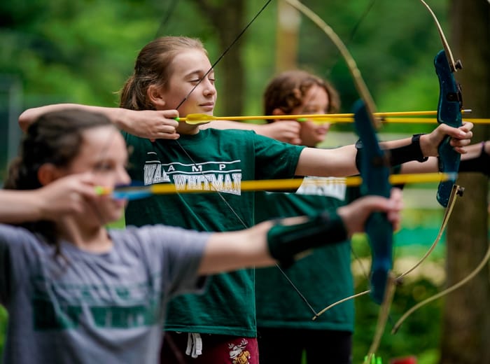 young girls shooting an arrow with a drawn back bow