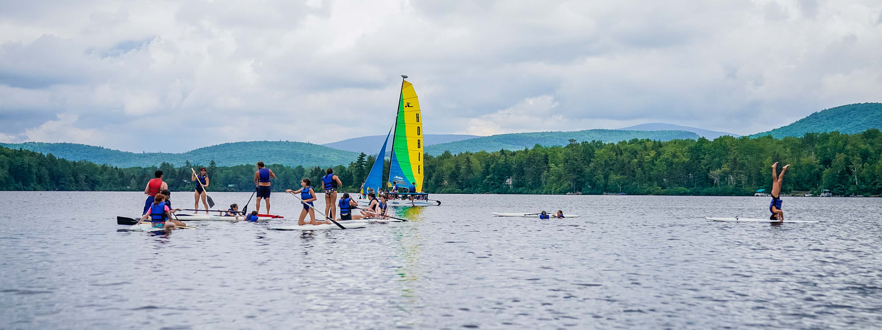 campers on sailboats and standing paddle boats on a lake