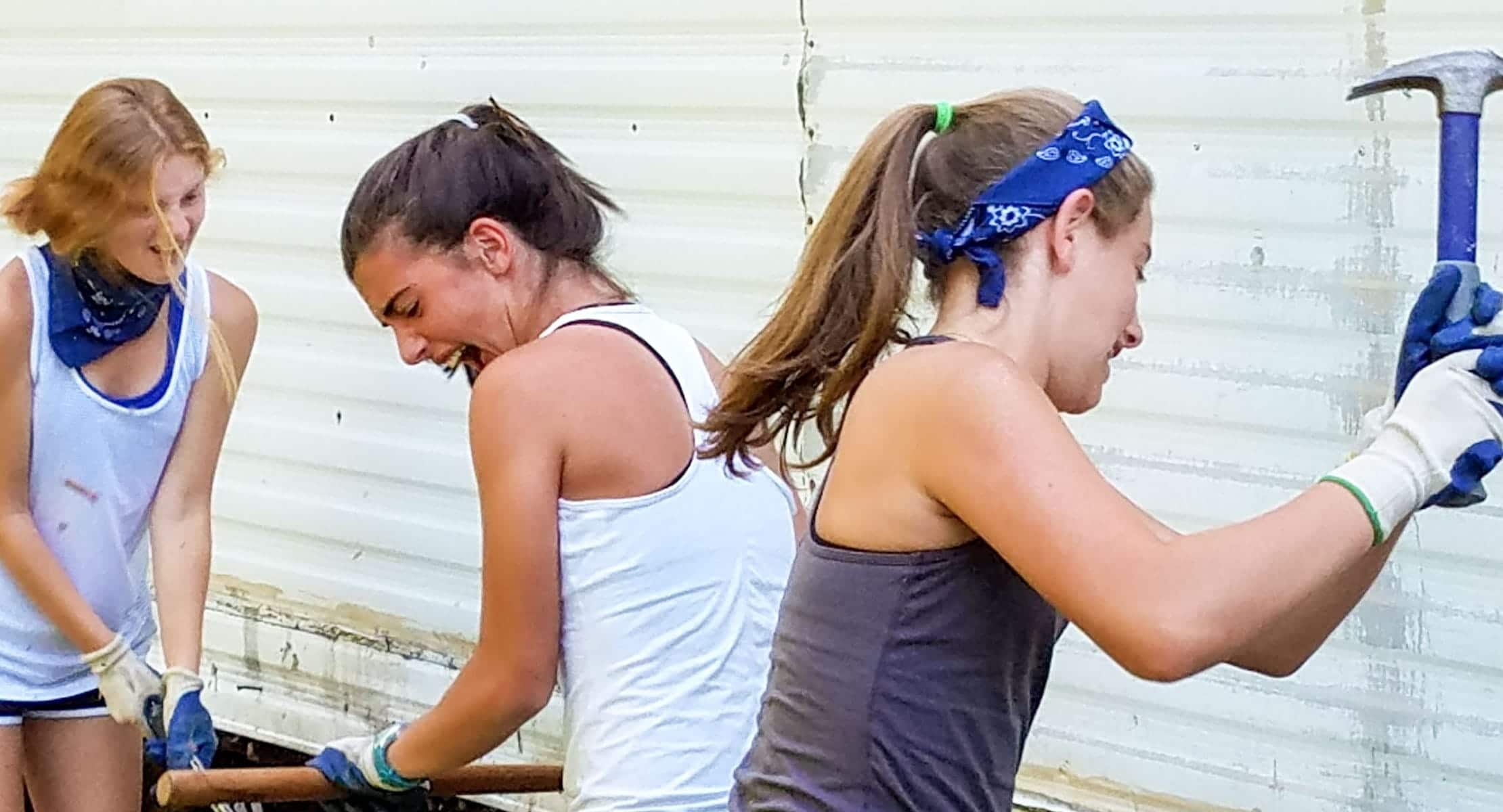 three young women hitting hammers against a house