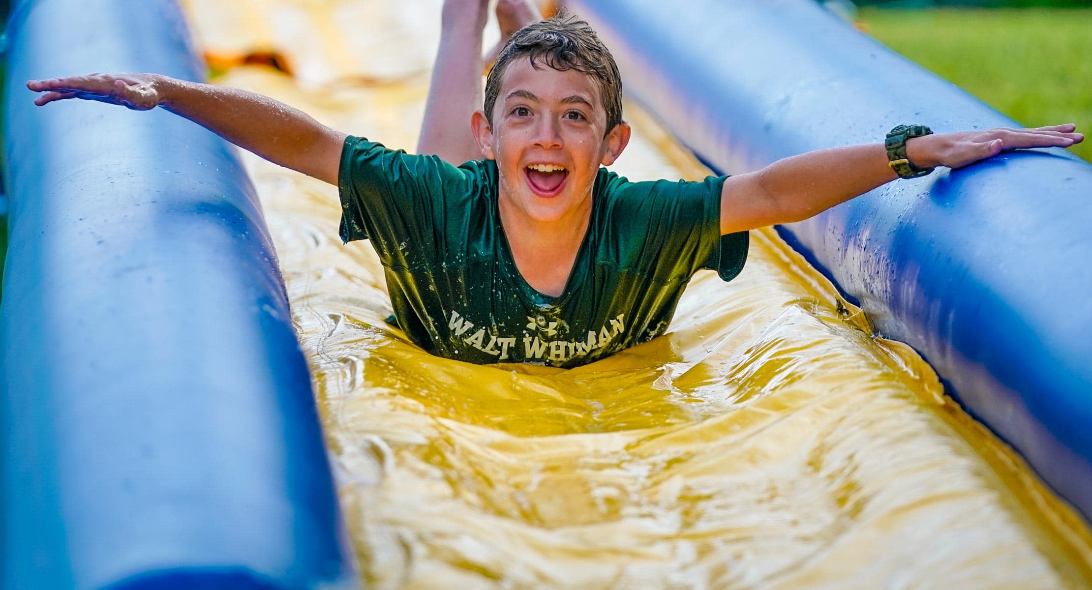 a young boy sliding on a slip n slide smiling at camera with arms outstretched