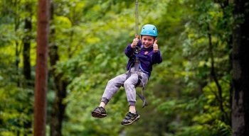 a young camper ziplining and giving a thumbs up