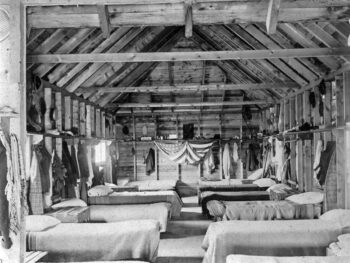 black and white photo of old fashion cabin with beds and an american flag