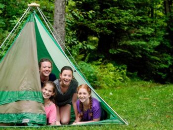4 young girls peaking out from a tent in a forest