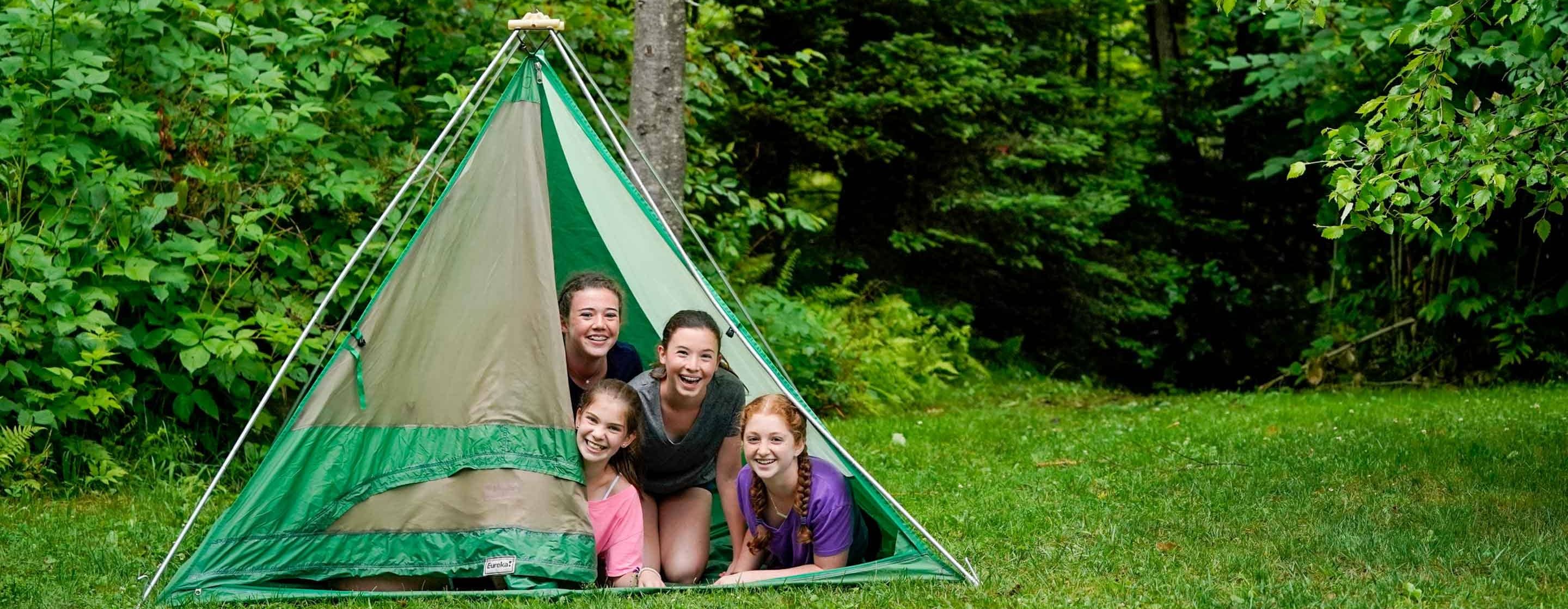 4 young girls peaking out from a tent in a forest