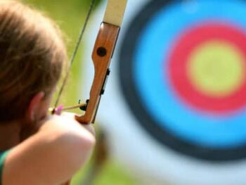 young girl with an arrow drawn back about to shoot at an archery target
